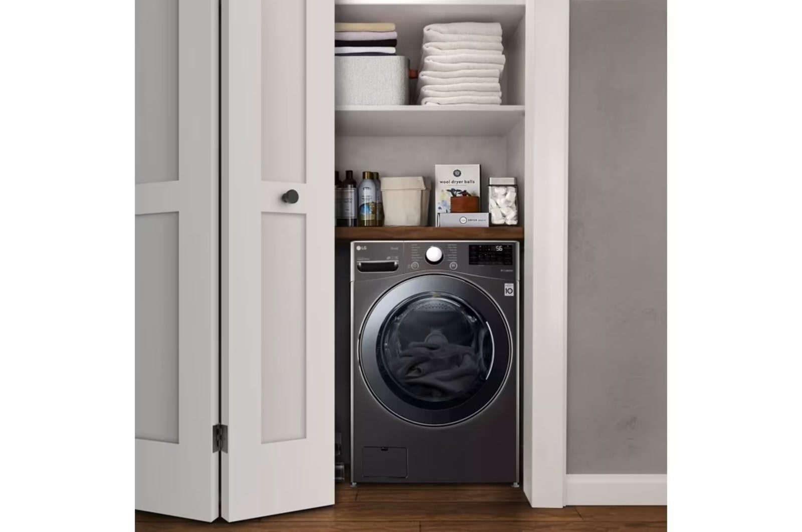Un lave-linge LG dans un petit placard doté d’étagères bien rangées contenant des serviettes et des produits de lessive, soulignant l’optimisation de l’espace.