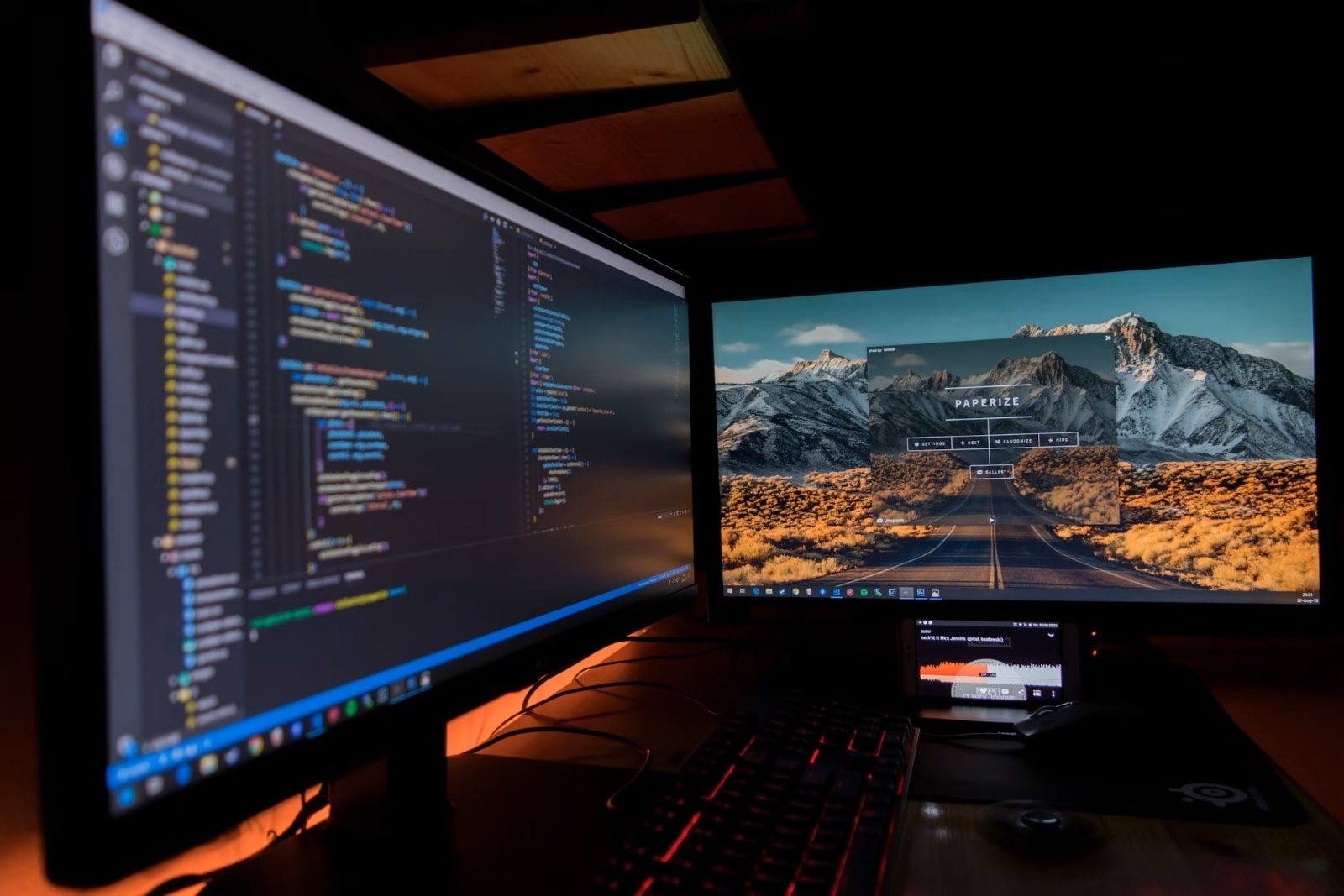 Deux moniteurs d'ordinateur affichant du code et un paysage de montagnes, utilisés pour le multitâche.