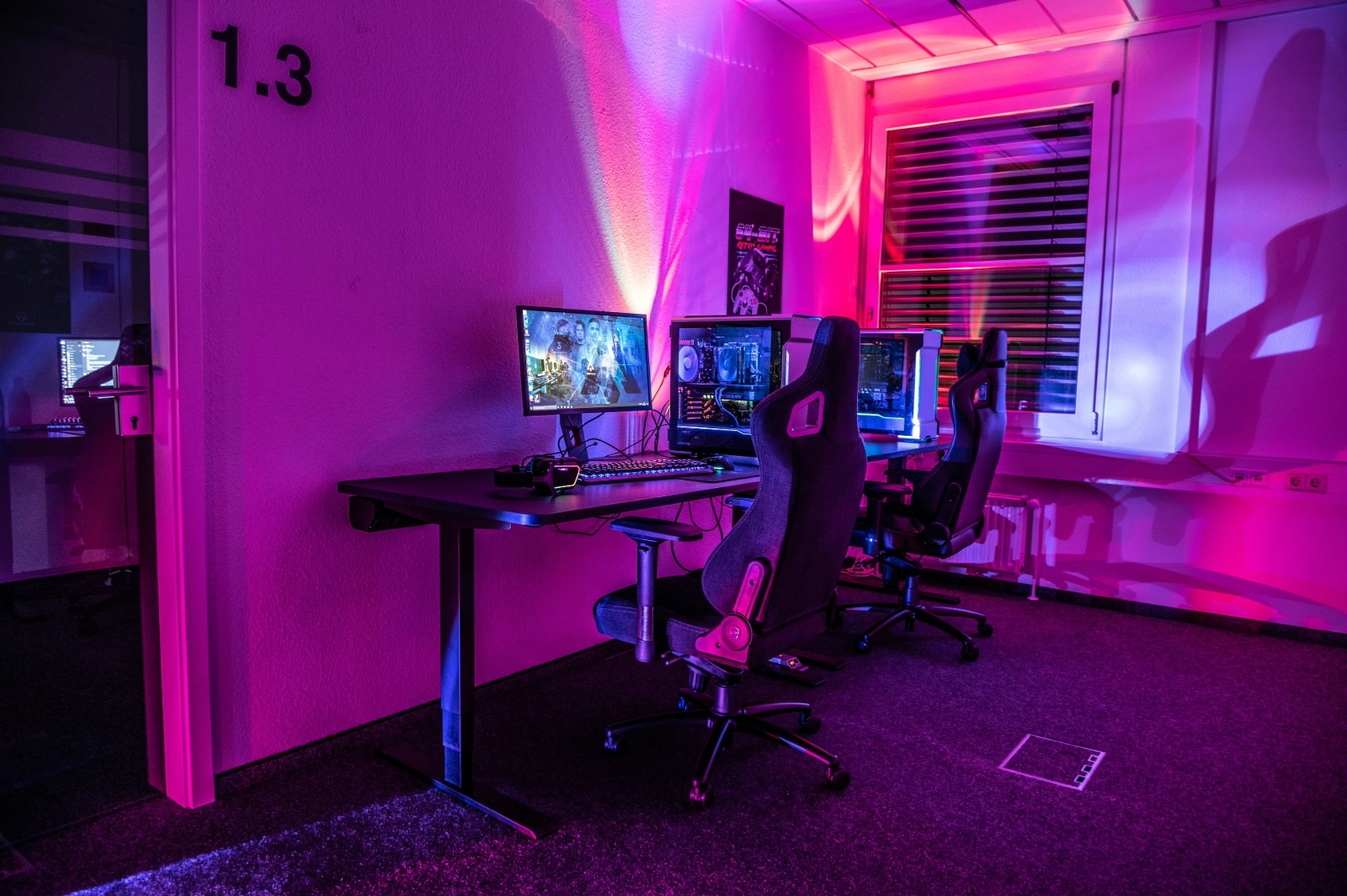 Une configuration de jeu avec un PC haute performance, un grand moniteur affichant un jeu futuriste, des haut-parleurs et des accessoires de jeu sur un bureau en bois, illuminé par un éclairage d'ambiance coloré.