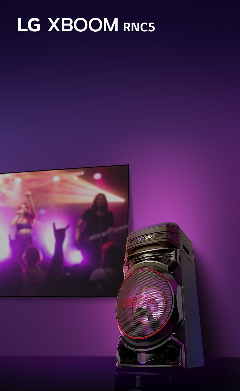 Χαμηλ? ?ποψη τη? δεξι?? πλευρ?? του LG XBOOM RNC5 υπ? χαμηλ? γων?α, σε μωβ φ?ντο.  Το φω? XBOOM ε?ναι επ?ση? μωβ. Σε μια οθ?νη τηλε?ραση? βλ?πουμε πλ?νο απ? μια συναυλ?α.