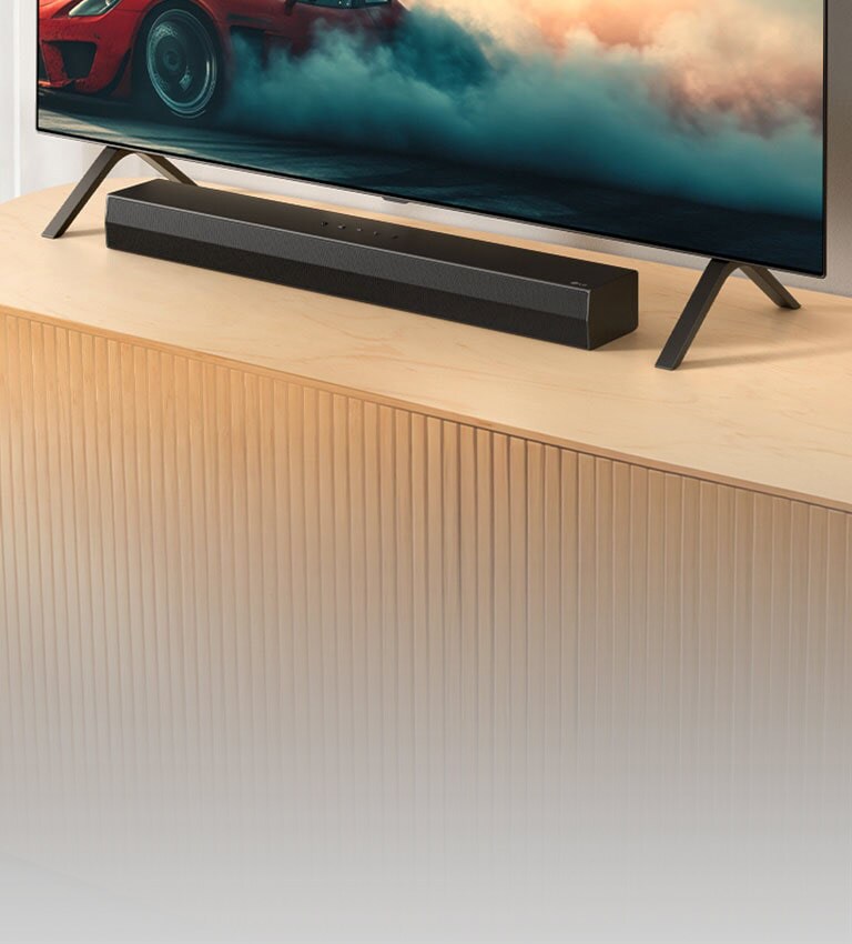Το LG Soundbar S20A τοποθετε?ται σε μια ξ?λινη κονσ?λα τηλε?ραση?, κ?τω απ? μια τηλε?ραση και αν?μεσα στι? β?σει? τη? τηλε?ραση?. Στην τηλε?ραση εμφαν?ζεται ?να κ?κκινο αυτοκ?νητο με καπν?.