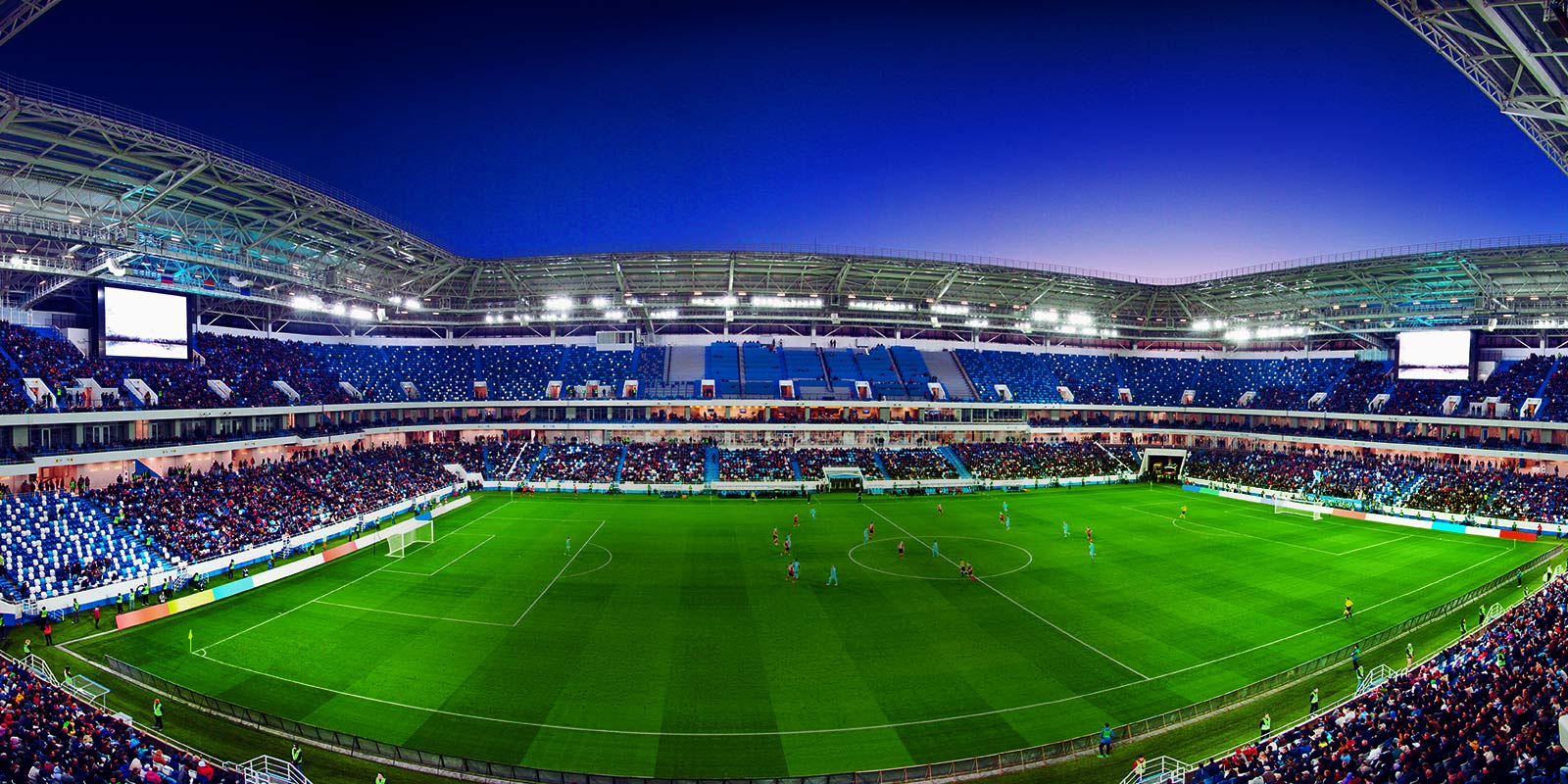 ?irokokutni prikaz nogometnog stadiona s punim tribinama i utakmicom u tijeku.