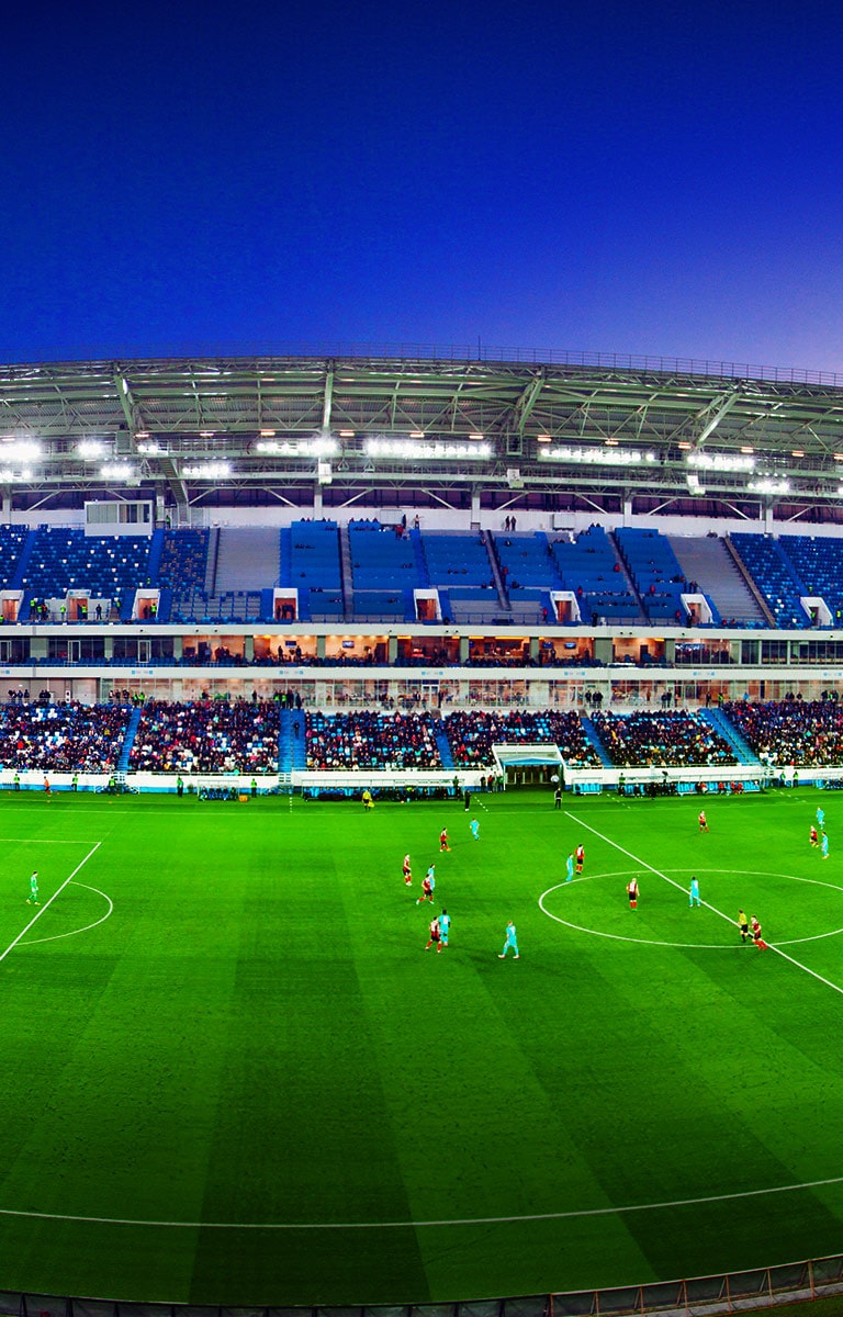 ?irokokutni prikaz nogometnog stadiona s punim tribinama i utakmicom u tijeku.