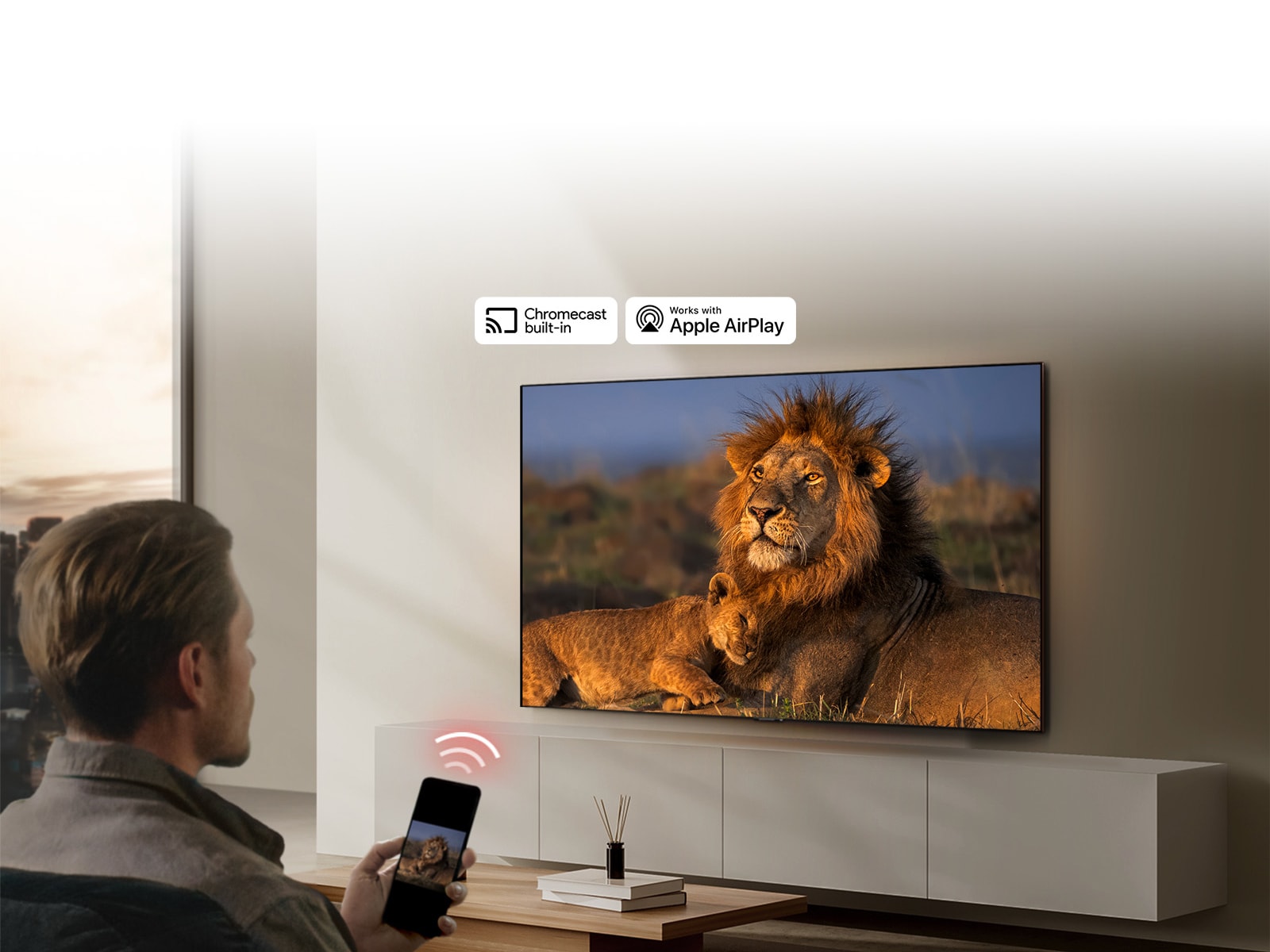 Televizor LG TV montiran na zidu dnevnog boravka, prikazuje se lav i mladun?e lava. U prvom planu se prikazuje mu?karac koji sjedi i dr?i mobitel u ruci na ?ijem se zaslonu vidi ista slika lavova. Grafi?ki prikaz tri neonsko crvene zakrivljene trake prikazuje se to?no iznad pametnog telefona usmjerenog prema televizoru.