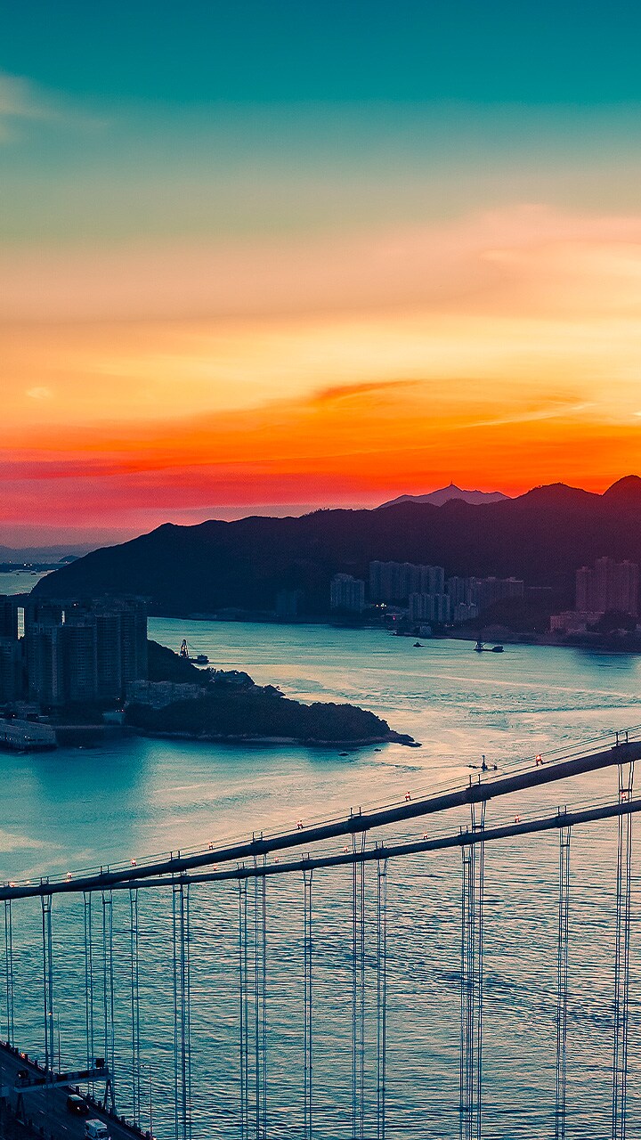 An ariel view of a coastal city with traffic driving over a bridge as the sun sets appears across the full screen. It is cropped and shown on an LG OLED television screen with the original colours unchanged.