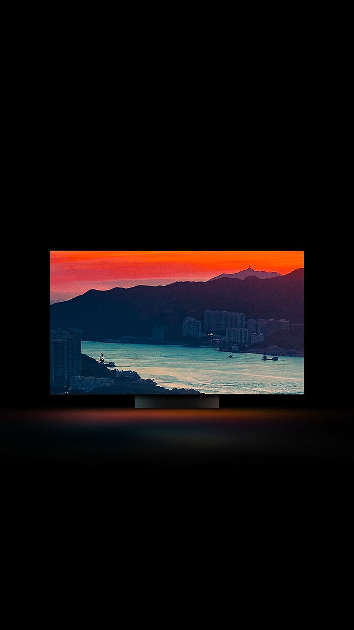 An ariel view of a coastal city with traffic driving over a bridge as the sun sets appears across the full screen. It is cropped and shown on an LG OLED television screen with the original colours unchanged.