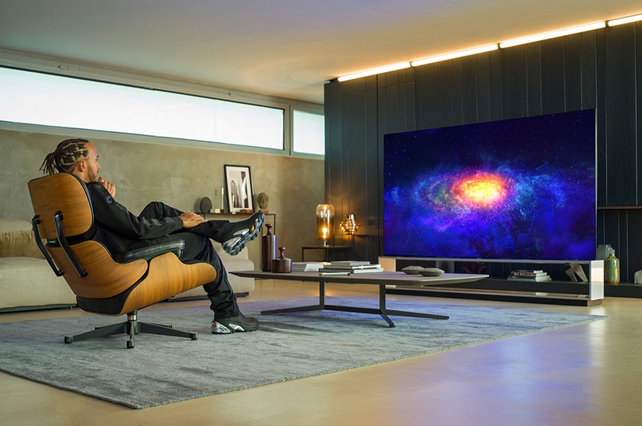 Lewis Hamilton che siede in poltrona, mentre guarda la TV OLED 8K ZX LG SIGNATURE.