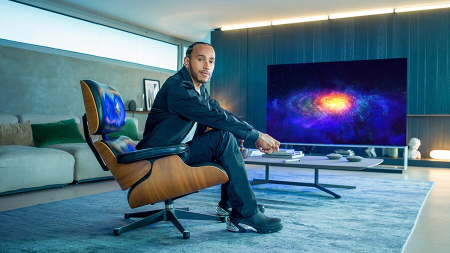 Lewis Hamilton che siede in poltrona e, dietro di lui, la TV OLED 8K LG SIGNATURE a fare da sfondo.