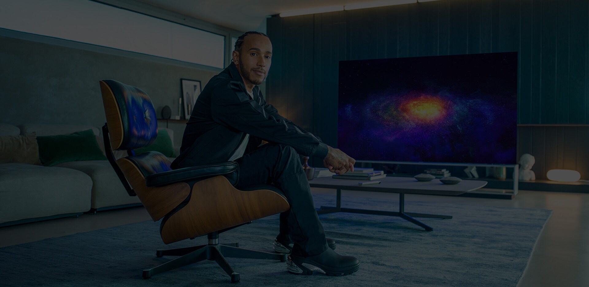 Lewis Hamilton che siede in poltrona e, dietro di lui, la TV OLED 8K LG SIGNATURE a fare da sfondo.