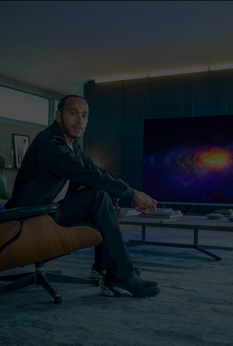 Lewis Hamilton che siede in poltrona e, dietro di lui, la TV OLED 8K LG SIGNATURE a fare da sfondo.