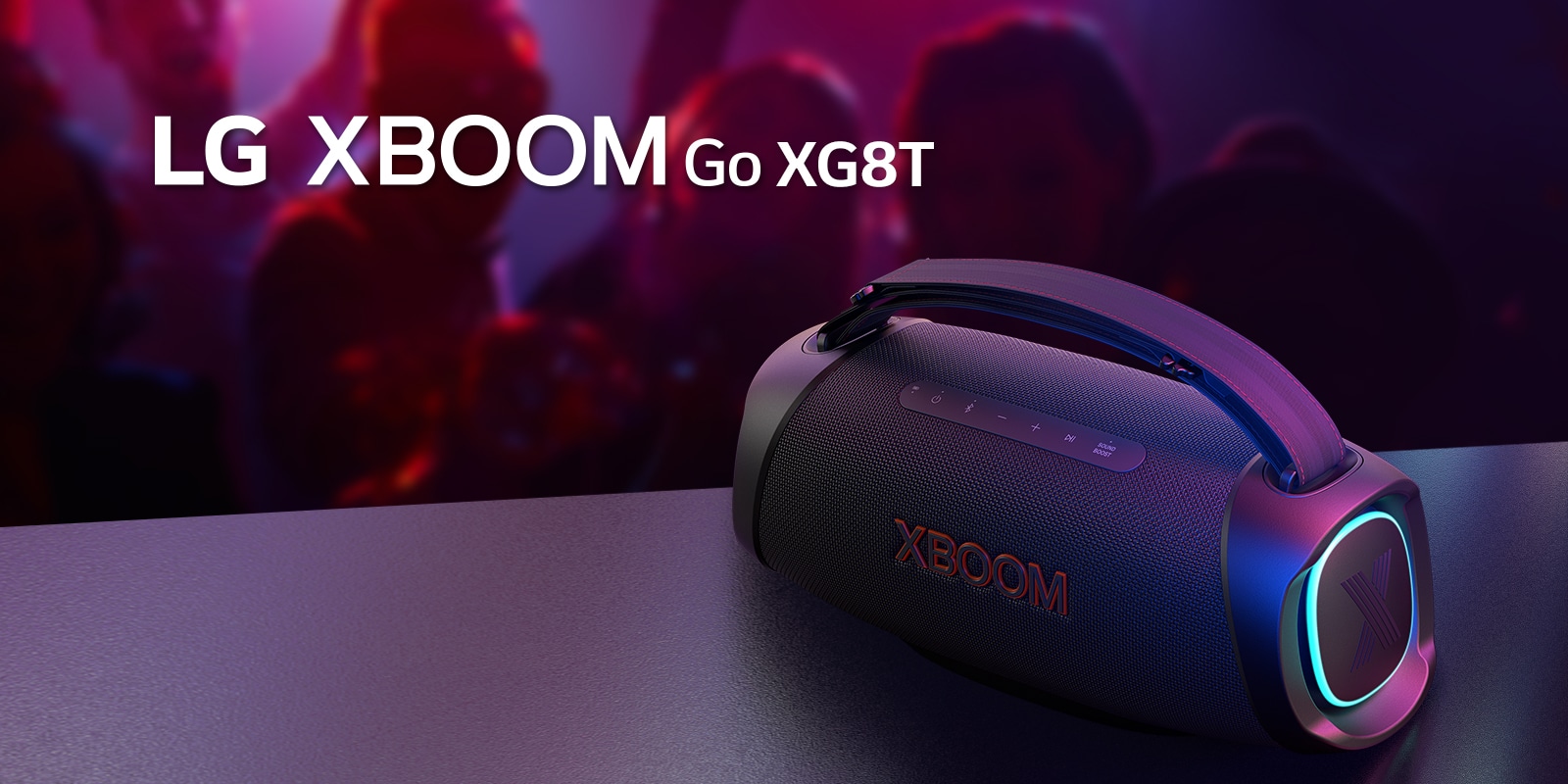 LG XBOOM Go XG8T pad?tas ant metalinio stalo su ?jungtu oran?iniu ap?vietimu. U? stalo ?mon?s m?gaujasi muzika.