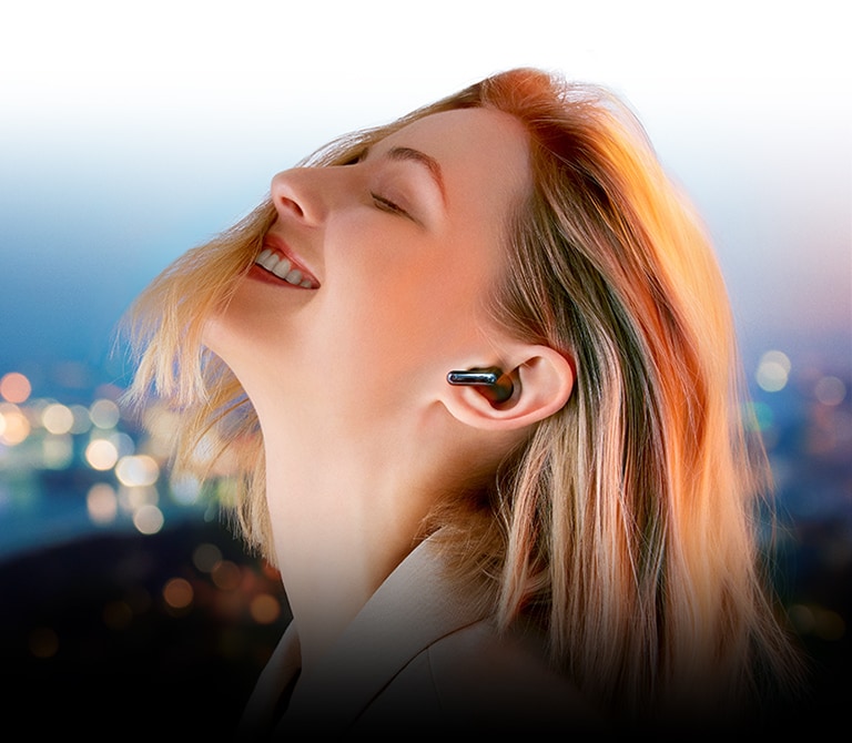 U? sakinio ??spūdingas garsas“ pateikiamas moters, naudojan?ios ausines ?TONE Free“ naktinio miesto fone ir panirusios ? muzik?, vaizdas.