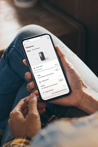 Bilde som viser en app som lar deg manipulere kj?leskapet til ? holde telefonen i h?nden.