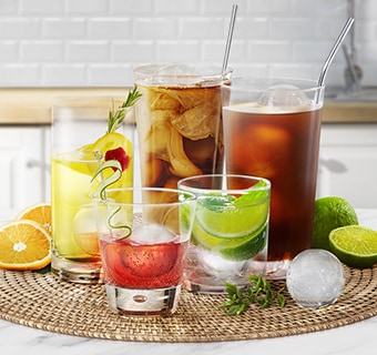 En person holder en kopp som inneholder en drink i den ene h?nden og en formet isball i den andre.