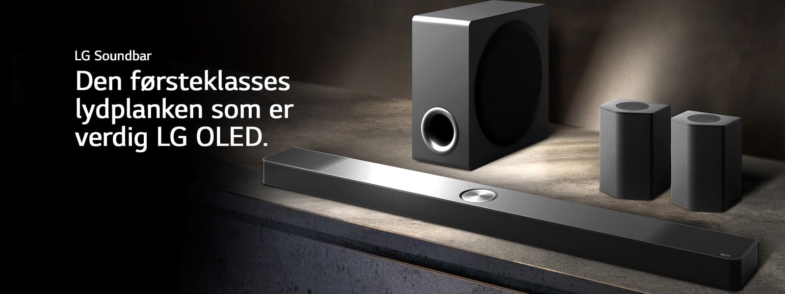 LG Soundbar, bakh?yttalere og subwoofer er plassert i et vinklet perspektiv p? en brun trehylle i et svart rom, innhyllet i m?rke med lys som bare kaster over lydanlegget.