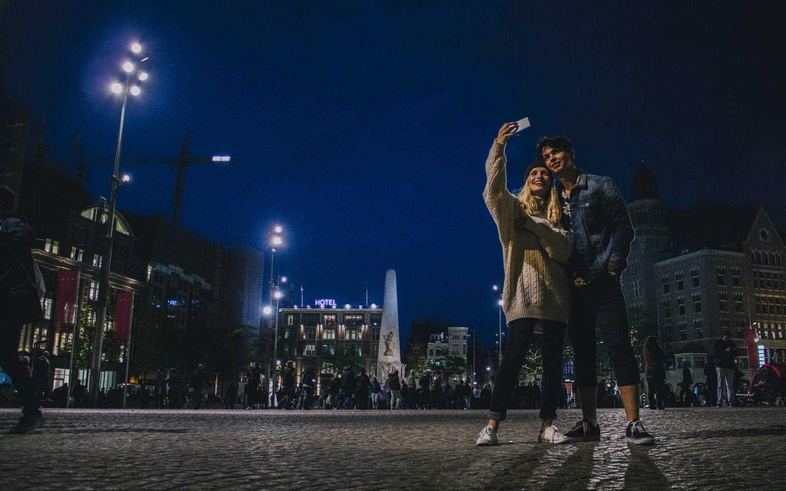 U?miechni?ta para robi selfie smartfonem LG K40 noc? na tle krajobrazu miasta