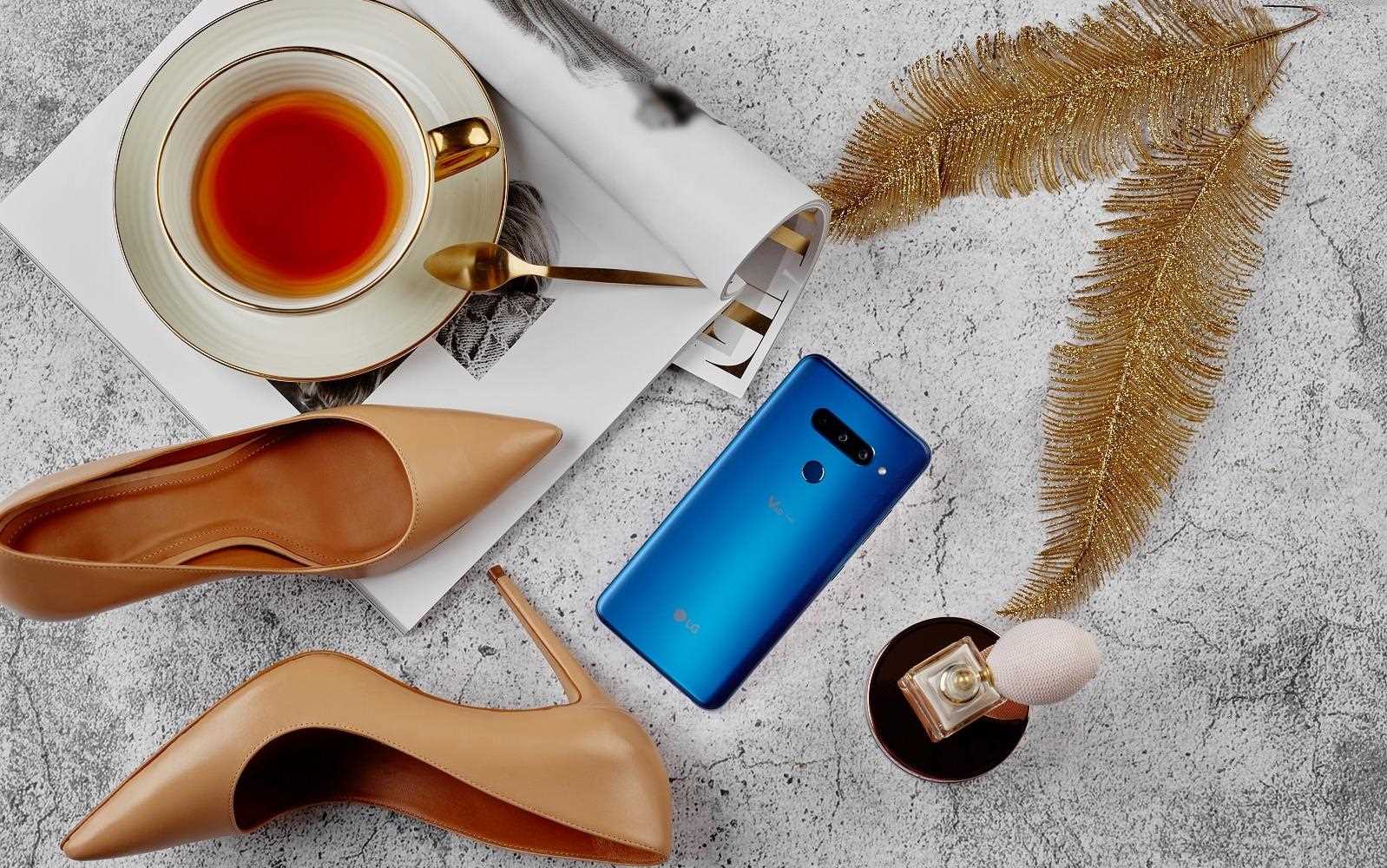 Stylowy smartfon LG V40 w otoczeniu z?otych piór, eleganckich szpilek, fili?anki z herbat? i perfum