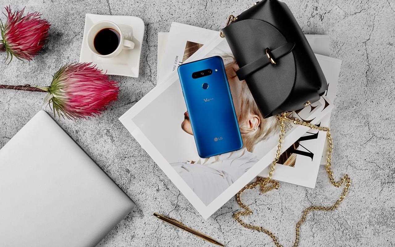 Niebieski, elegancki smartfon V40 le??cy na magazynach z mod?, obok skórzanej torebki, kwiatów i fili?anki z kaw?