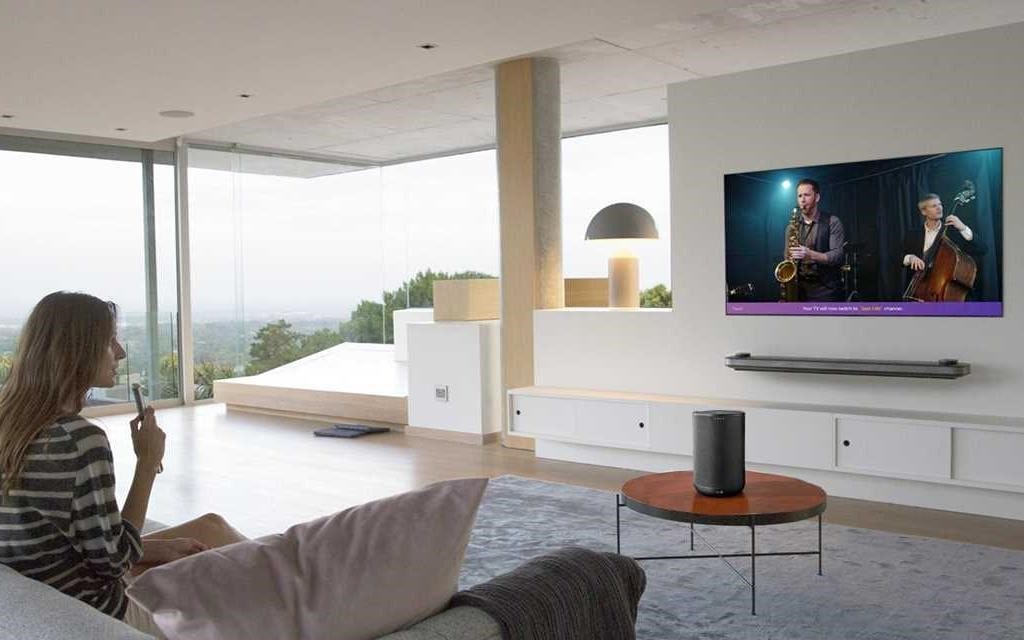 Kobieta siedz?ca w swoim salonie, za pomoc? pilota LG, rozmawia z jej telewizorem LG OLED W8.