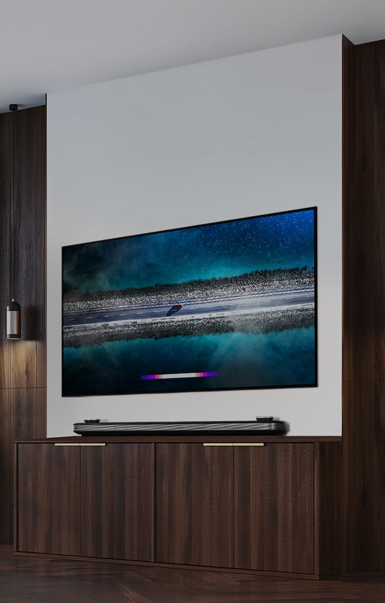 LG SIGNATURE OLED TV W9 este atarnat pe perete ?i o canapea este a?ezat? chiar ?n fa?a televizorului, cu cerul albastru de pe fereastr?.