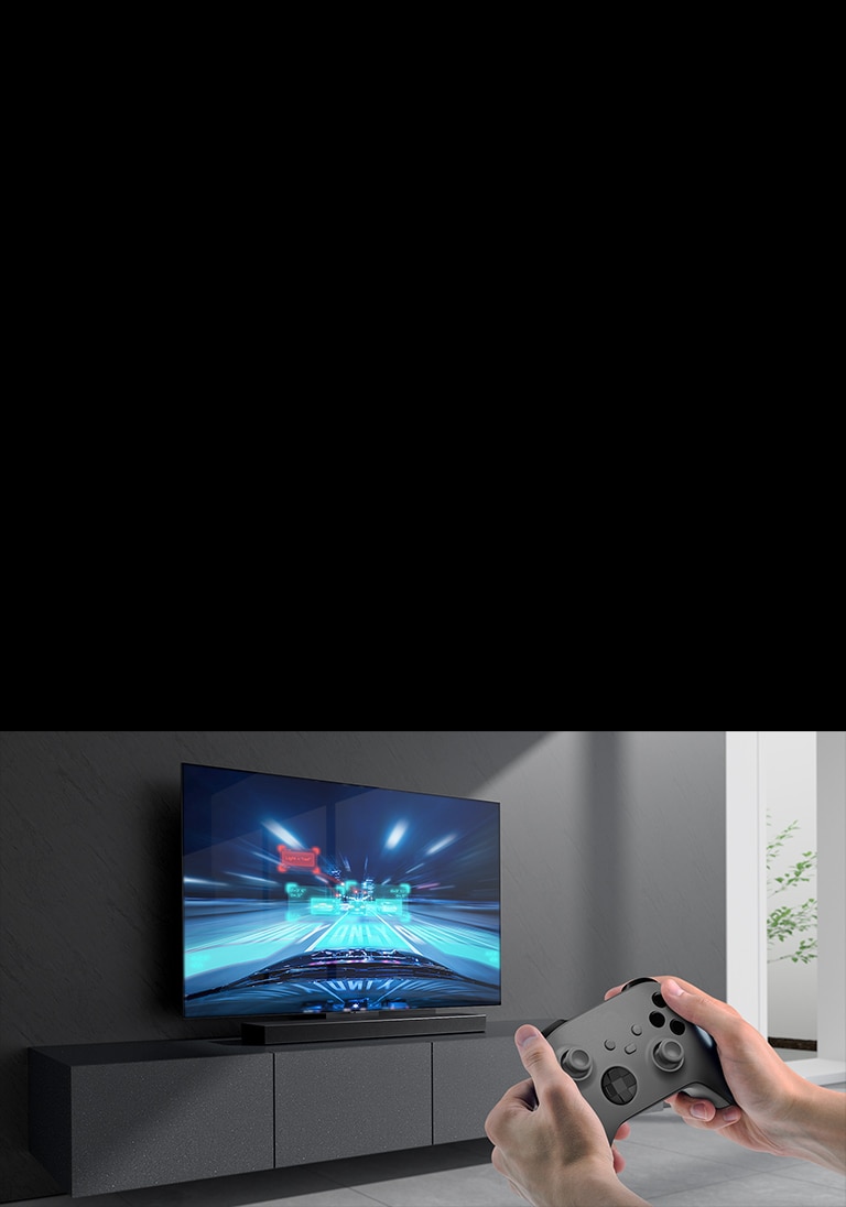 Sound Bar zvu?nik na elementu i scena iz trka?ke igre na televizoru povezanom sa Sound Bar zvu?nikom. Igra?ka konzola se nalazi u donjem desnom uglu slike i dr?e je dve ruke.