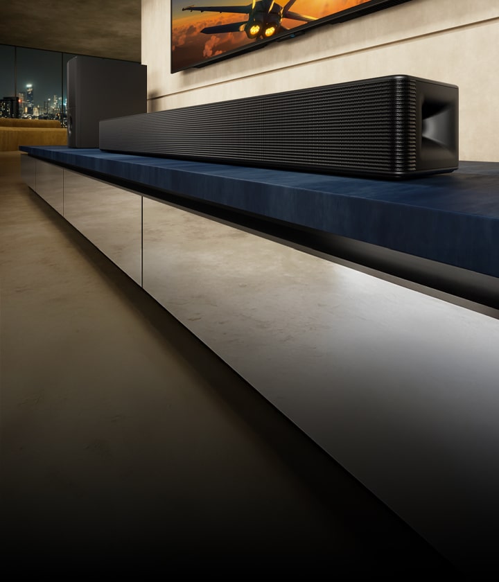 LG Soundbar SH5A i njegov niskotonac nalaze se na plavoj TV komodi u dnevnoj sobi. Iznad Soundbar ure?aja je delimi?no prikazan TV sa slikom letelice.