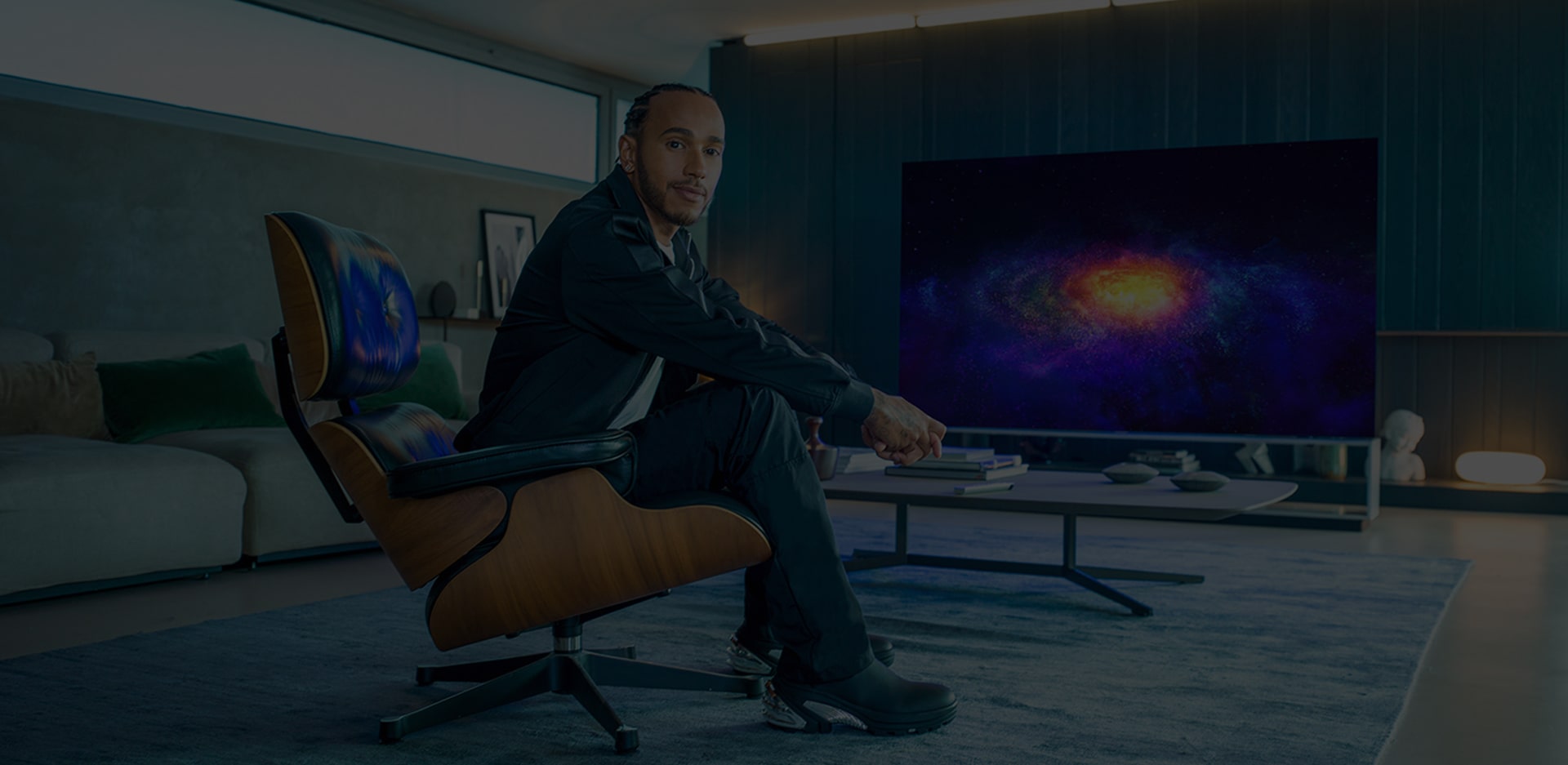 Льюис Хэмилтон сидит в кресле напротив телевизора LG SIGNATURE OLED 8K.