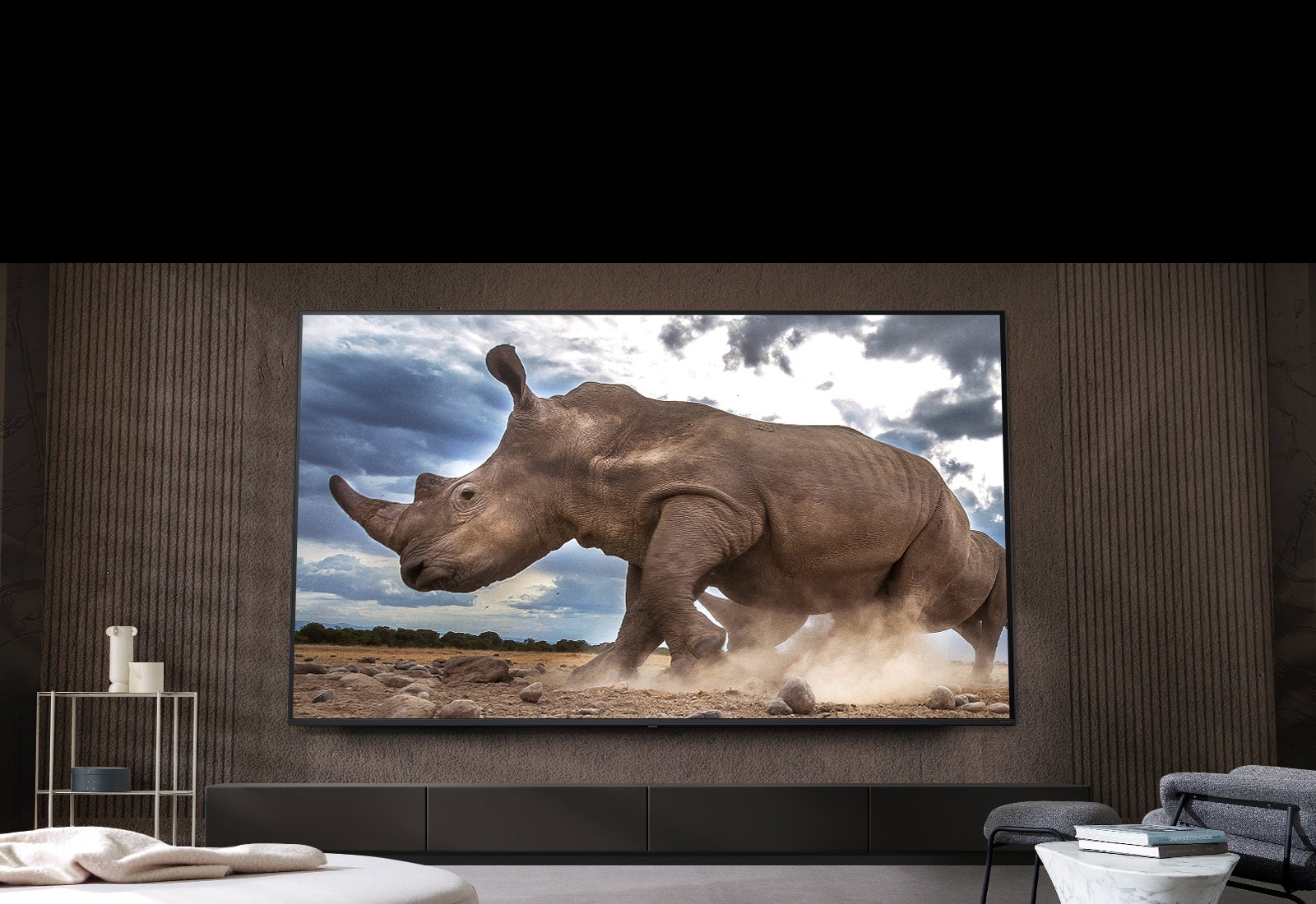 Na ultra ve?kom televízore LG na hnedej stene obyva?ky obklopenej modulárnym nábytkom v krémovej farbe sa zobrazuje nosoro?ec v prostredí safari.
