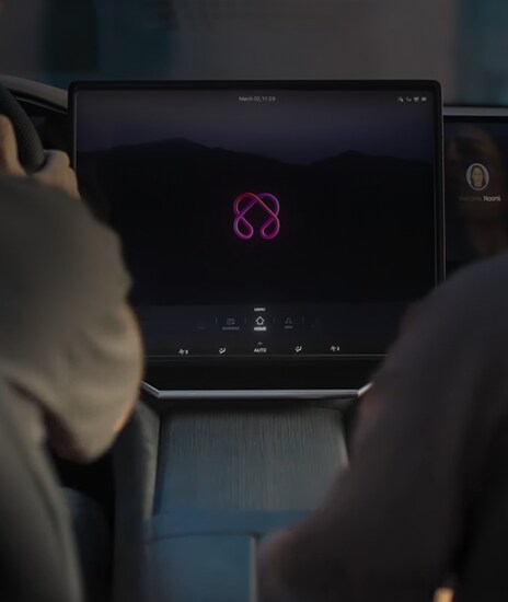 Inside a car with two people sitting, the LG AI logo is glowing on the screen.