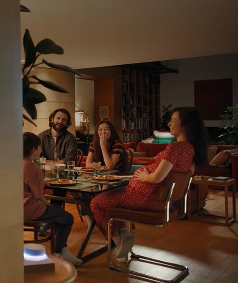 People are sitting around the table, smiling, and the LG ThinQ is turned on above the table on the left.