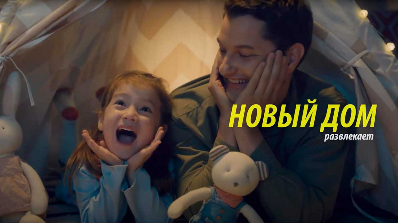 Дочь смотрит телепрограмму в уютной домашней обстановке и с широкой улыбкой на лице. Ее отец смотрит на нее счастливой. Заголовок гласит, что новый дом развлекает вас.